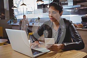 Woman with phone using laptop in cafe