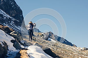 A woman photographer with camera and backpack in a winter jacket with fur stands on the snow mountain in Switzerland. Fluela pass