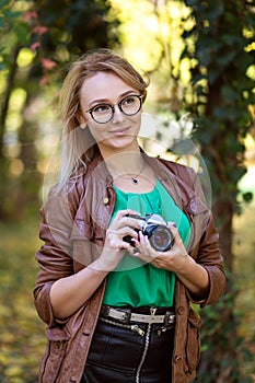Woman photographer with hipster style glasses taking pictures in park with retro camera.