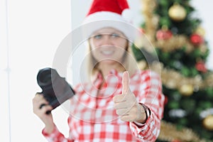 Woman photographer is holding a camera and thumbs up gesture against background of New Year tree
