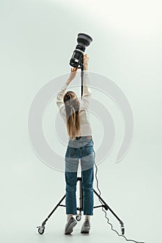 Woman photographer in a photo studio adjusts the light with a reflector on a white background. Backstage