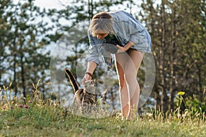 Woman photographer plays with lonely cat walking on forest meadow against blurry green trees