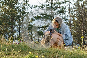 Woman photographer plays with lonely cat walking on forest meadow against blurry green trees