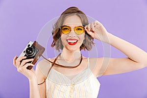 Woman photographer posing isolated over purple wall background holding camera.