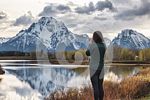 Woman Photographer at River surrounded by Trees and Mountains in American Landscape.