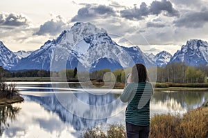 Woman Photographer at River surrounded by Trees and Mountains in American Landscape.