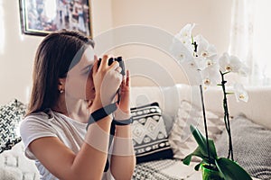 Woman photographer takes picture of blooming orchid using camera. Freelancer works from home during covid