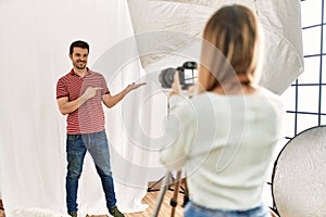Woman photographer talking pictures of man posing as model at photography studio amazed and smiling to the camera while presenting