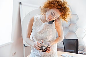 Woman photographer using vintage camera and talking on mobile phone