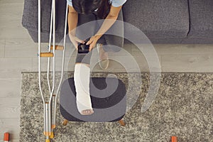 Woman photographing her leg in a plaster cast for an online consultation with a doctor.