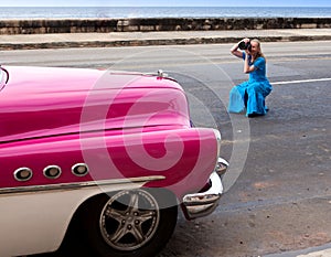 The woman photographs the ancient car on the Malecon street January 27, 2013 in Old Havana, Cuba