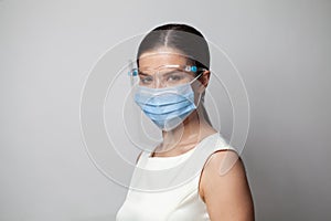 Woman physician in face shield looking at camera. Portrait of female doctor or nurse in medical mask and goggles on white