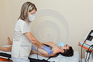 woman physiotherapist with mask does a diathermy to a man whith a chronic pain