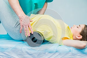 Woman at the physiotherapy doing physical exercises with her therapist, they using a massage roll. A chiropractor treats patient`