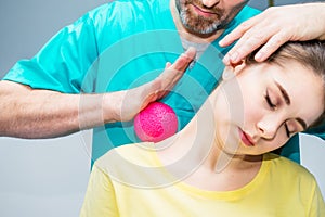 Woman at the physiotherapy receiving ball massage from therapist. A chiropractor treats patient`s shoulder, neck in medical offic