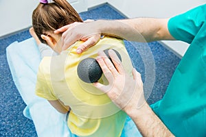 Woman at the physiotherapy receiving ball massage from therapist. A chiropractor treats patient`s thoracic spine in medical offic