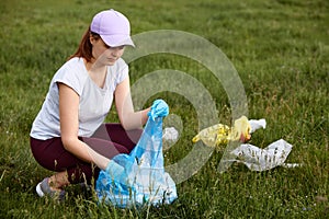 Woman picking up plastic bottles and rubbish from meadow, environmental activist collecting plastic garbage, volunteer picking up