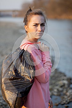 Woman picking up trash and plastics cleaning the beach with a garbage bag. Environmental volunteer activist against