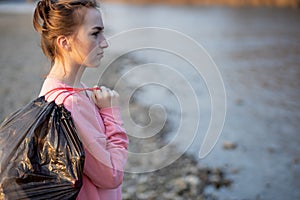 Woman picking up trash and plastics cleaning the beach with a garbage bag. Environmental volunteer activist against climate change