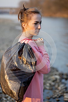 Woman picking up trash and plastics cleaning the beach with a garbage bag. Environmental volunteer activist against climate change