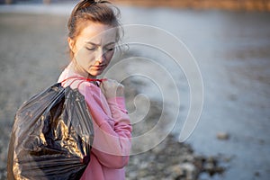 Woman picking up trash and plastics cleaning the beach with a garbage bag. Environmental volunteer activist against climate change