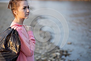 Woman picking up trash and plastics cleaning the beach with a garbage bag. Environmental volunteer activist against climate change