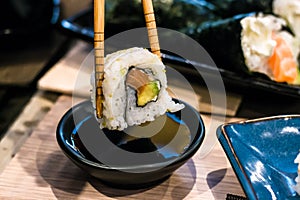 Woman picks up Uramaki sushi roll with fresh salmon, avocado and philadelphia cheese, covered with sesame seeds photo