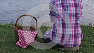 Woman with picnic basket sits by lake side close up