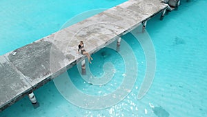 Woman on pier looking at stingray in sea on Maldives. Sting ray fishes swimming in blue ocean, aerial view