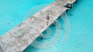 Woman on pier looking at stingray in sea on Maldives. Sting ray fishes swimming in blue ocean, aerial view