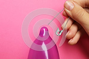 Woman piercing inflated condom with pin on background, closeup. Safe sex