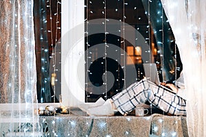 Woman in pijamas sitting on windowsill with laptop computer working from home.Winter mood.