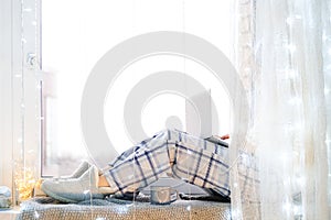 Woman in pijamas sitting on windowsill with laptop computer working from home.Winter mood.