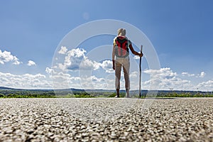 Woman with pilgrim stick and backpack barefoot on a road