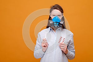 woman with pills and thermometer in hands in protective equipment in medical mask on yellow background, coronavirus pandemic, look