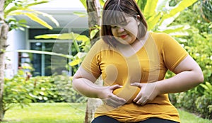 Woman pinches fat on her belly large size while sitting in the garden at home. Upset female suffering from extra