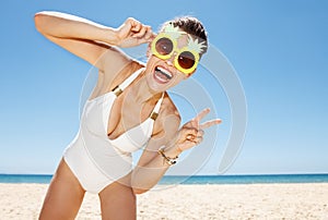 Woman in pineapple glasses showing victory gesture at beach