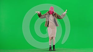 Woman in pink balaclava, tiger coat and evening dress gracefully dancing oriental dance. Freak woman on a green