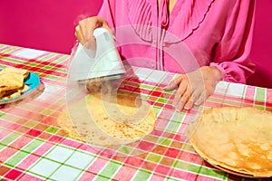 Woman in pink blouse ironing pancake on plaid tablecloth. Meme featuring unexpected ways to prepare food through humor.