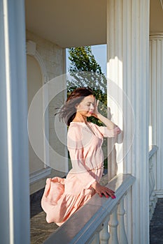 Woman in pink dress with hair flying on wind standing on stairs outdoors