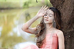 a woman in pink dress looking tired by her hand gesture and leaning to a tree