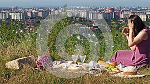 A woman in pink dress sits on a picnic in a park with panoramic view