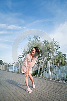 Woman in pink dress standing on river bank with hair flying on wind, blue sky background