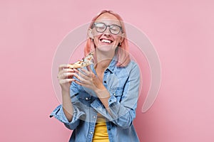 Woman with pink dyed hair and glasses eating a piece of pizza