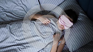 woman in a pink eye mask lies under a blanket in a bed and suffers from insomnia.