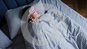 woman in a pink eye mask lies under a blanket in a bed and suffers from insomnia.