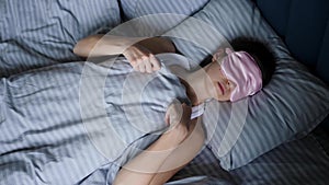 woman in a pink eye mask lies under a blanket in a bed and suffers from insomnia.