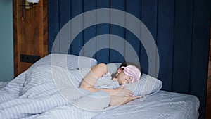 woman in a pink eye mask lies under a blanket in a bed and suffers from insomnia.