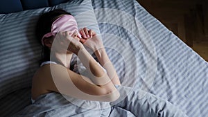 woman in a pink eye mask lies under a blanket in a bed and suffers from insomnia.