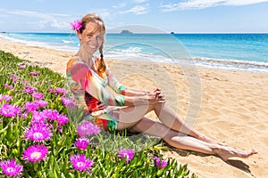 Woman with pink flowers on sandy beach with blue sea